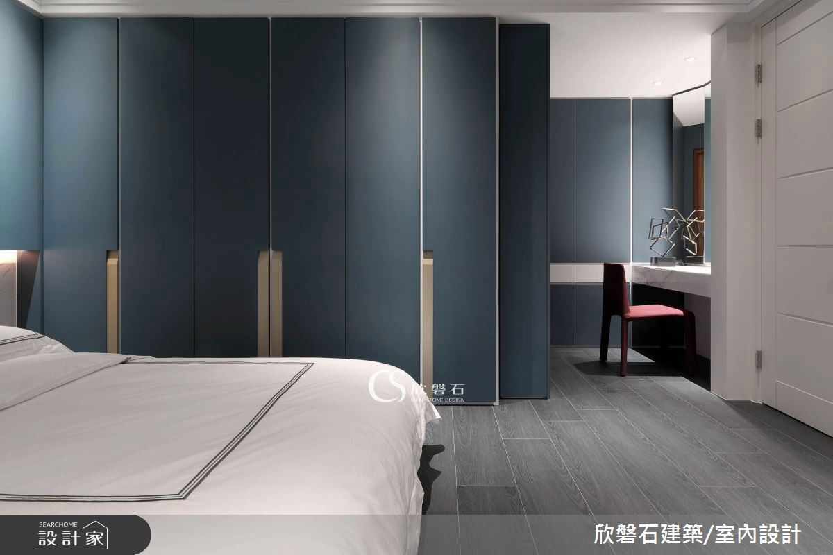 次臥以樑化出小客廳中起居與書房場域，整面白色拉門隱藏了以畸零角落建構的吧檯與收納空間，釋放視覺感受退以室外綠意景致為主角。睡眠區以白色大理石為底衍生懸空床頭櫃，立面承載搭配烤漆金隱藏式把手設計的墨藍色烤漆櫃體，延伸入內，梳妝區以卡拉拉白銀狐石材腰帶設計裝飾，石材導角抽屜與隱藏式鏡子，呈現細緻工藝與色彩的美學構思。