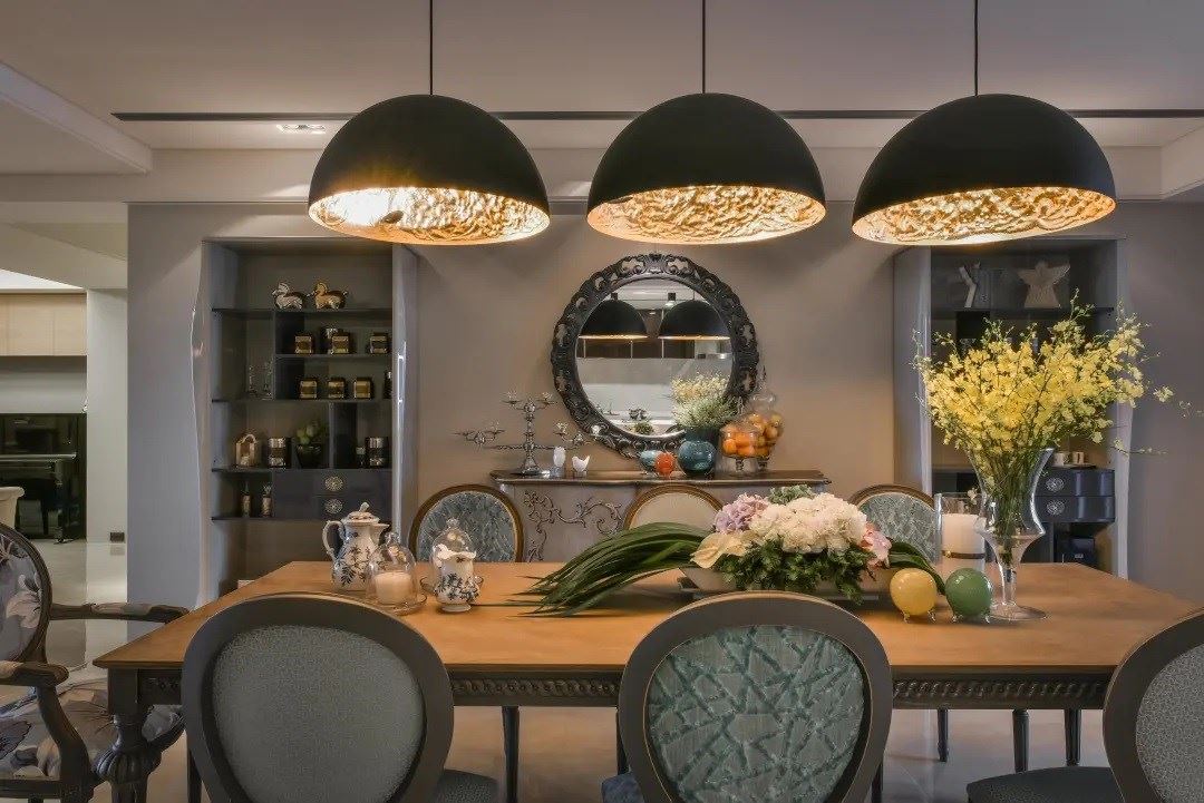 弧形照明的映照下，晕黄的光感让餐厅增添温度，映衬出后方以镜面、矮柜与展示收纳的端景美学。